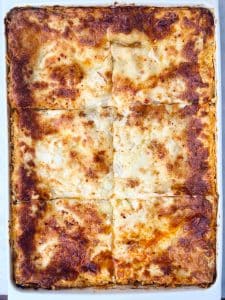Homemade lasagna baked until bubbling and golden, cut into neat squares in a white casserole dish.