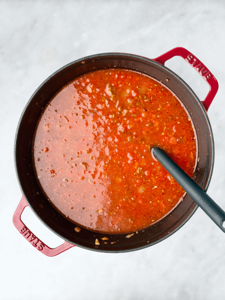 Rich tomato base for lasagna soup simmering in a red Dutch oven with ground beef and broth.