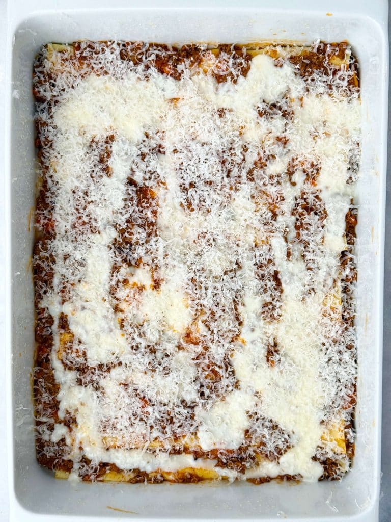 Partially assembled lasagna with layers of bolognese, béchamel sauce, and grated cheese in a white baking dish.
