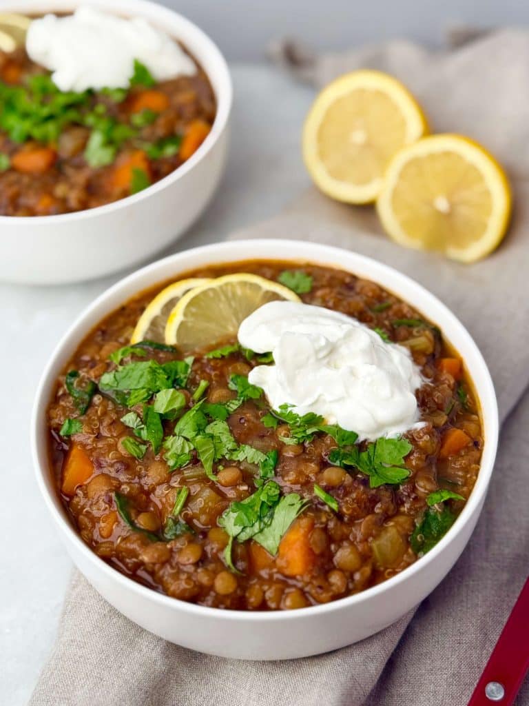 Low-calorie high-protein lentil soup in a white bowl topped with fresh cilantro, lemon slices, and a dollop of Greek yogurt.
