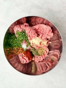 Ground turkey mixed with sage, thyme, garlic, and spices in a metal bowl for maple sage sausage patties.