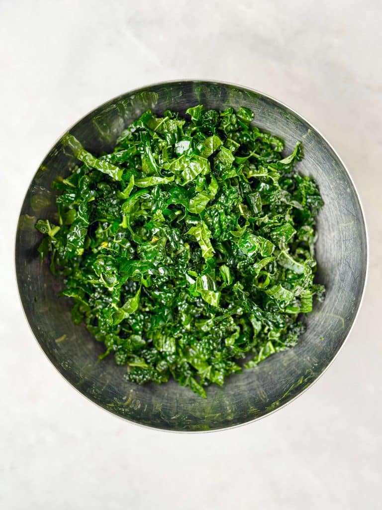 Bowl of freshly massaged kale with olive oil, ready to mix into warm butter bean salad.