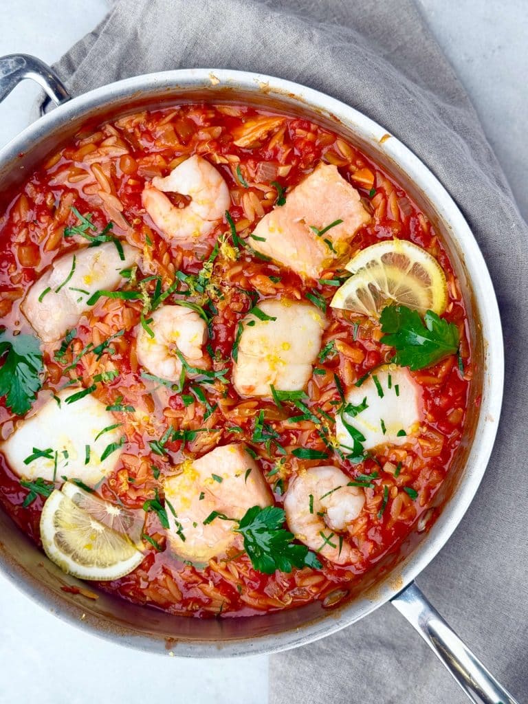 Mediterranean poached fish with shrimp and couscous in a vibrant spicy tomato sauce, topped with lemon and parsley.