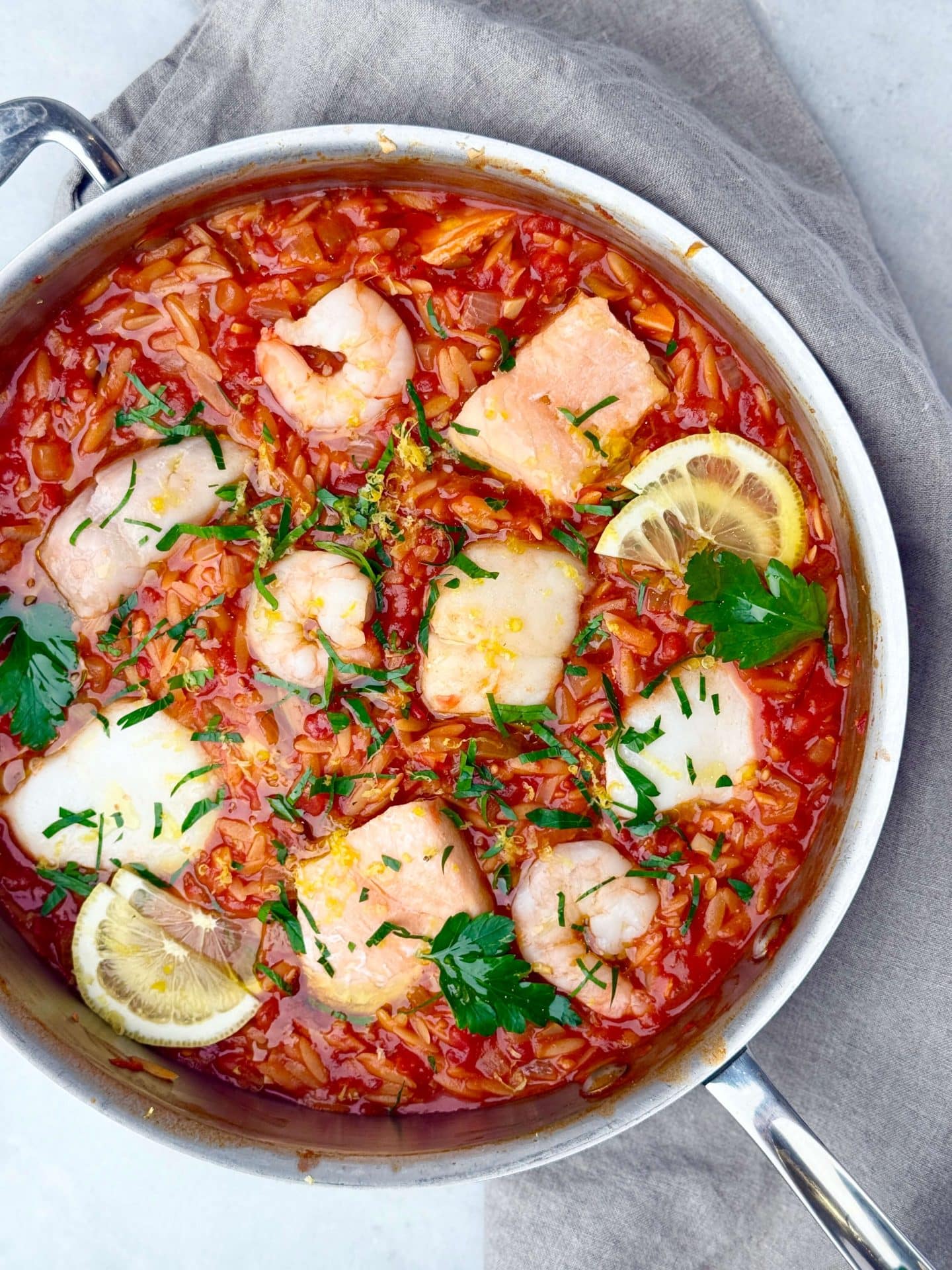 Mediterranean poached fish with shrimp and couscous in a vibrant spicy tomato sauce, topped with lemon and parsley.