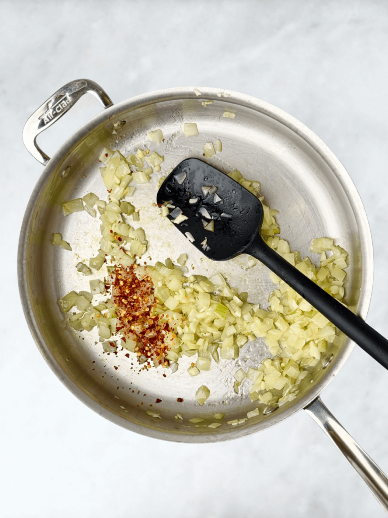 Sautéing onions, garlic, and chili flakes in olive oil to start the Mediterranean poached fish in spicy tomato sauce.