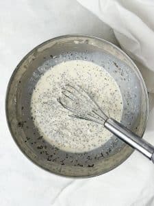 Chia seeds being whisked into dairy free milk and protein mixture in a metal bowl to make high protein chia seed pudding.