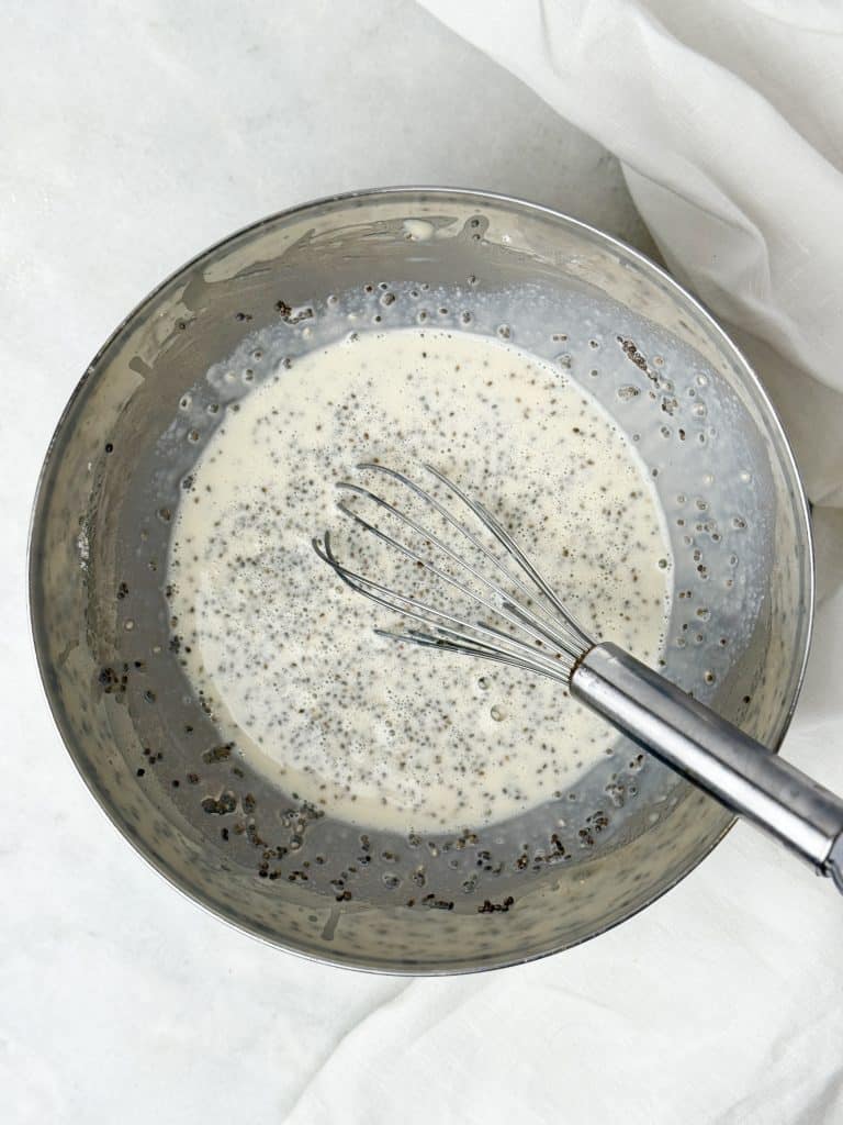 Chia seeds being whisked into dairy free milk and protein mixture in a metal bowl to make high protein chia seed pudding.