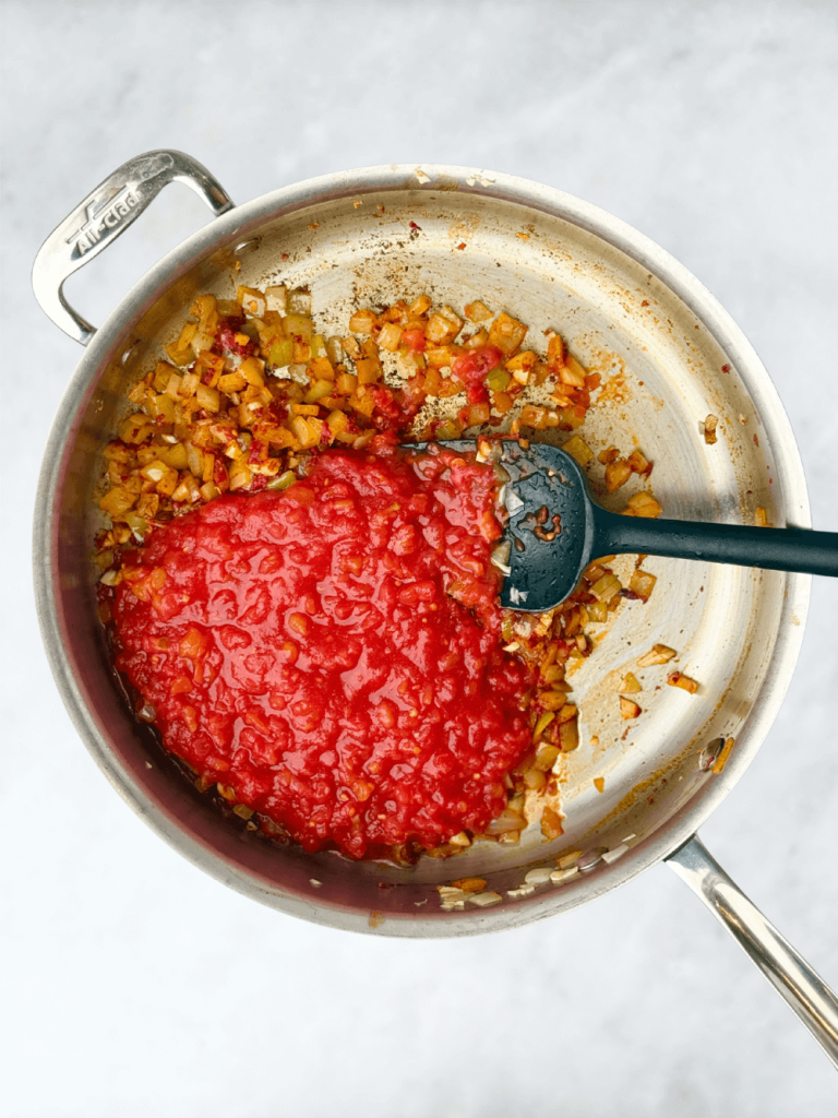 Stirring crushed tomatoes into the garlic and spice mixture to create a rich tomato base for Mediterranean poached fish.