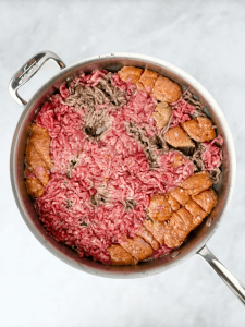 Ground beef and Italian sausage pressed flat in a skillet to begin browning for bolognese sauce.