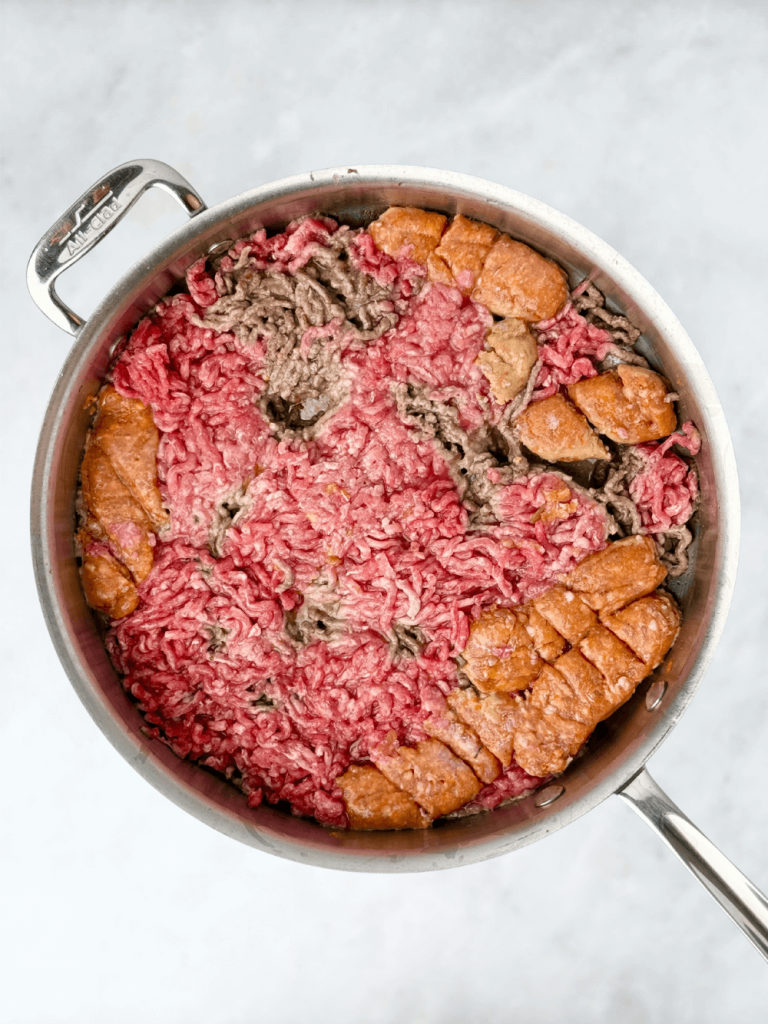 Ground beef and Italian sausage pressed flat in a skillet to begin browning for bolognese sauce.