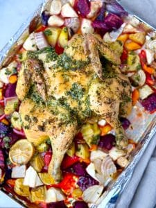 Whole oven roasted spatchcock chicken resting on a sheet pan surrounded by caramelized beets, carrots, and parsnips.