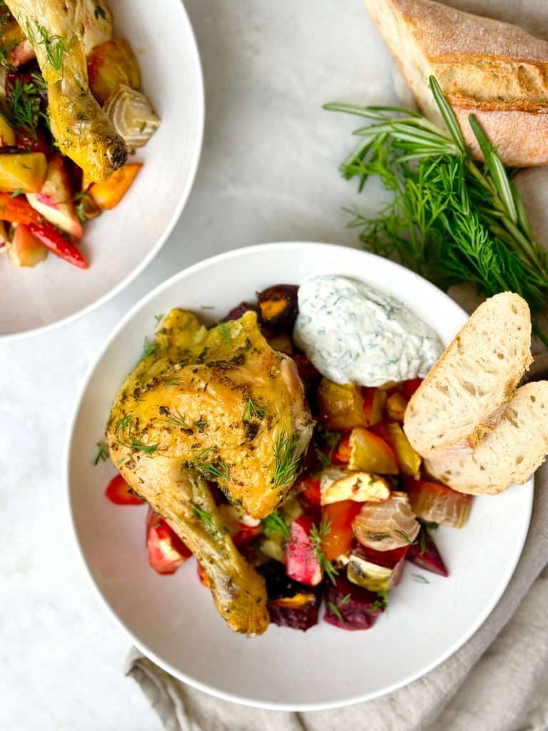 Two bowls of oven roasted spatchcock chicken and roasted root vegetables with lemon yogurt sauce and crusty bread.