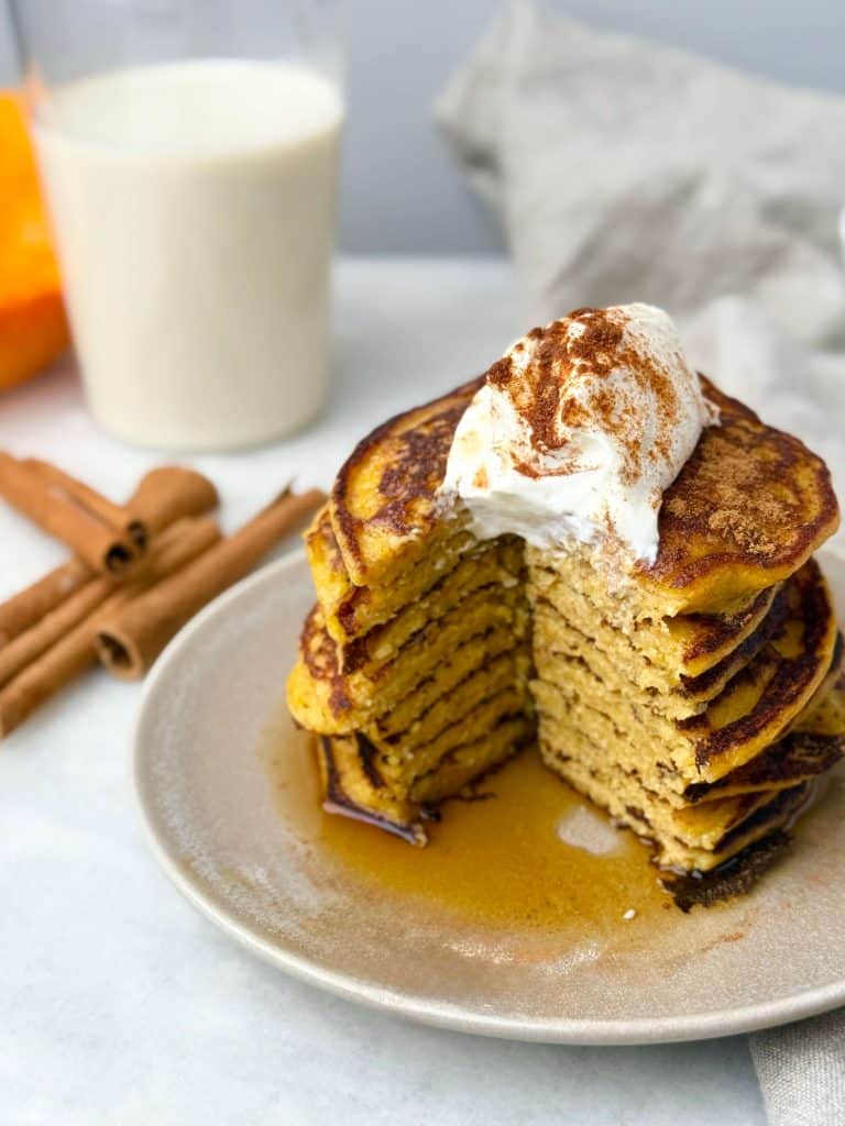 Stack of pumpkin protein pancakes with a cut section showing fluffy texture, topped with yogurt and syrup.