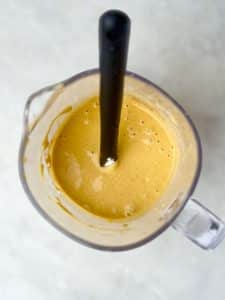 Pumpkin protein pancake batter blended until smooth in a glass blender with a black spatula on a light countertop.