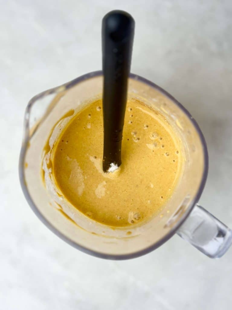 Pumpkin protein pancake batter blended until smooth in a glass blender with a black spatula on a light countertop.