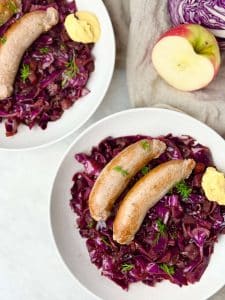 Plates of red cabbage with sausage, served with mustard and fresh dill in a cozy German-style dinner setting