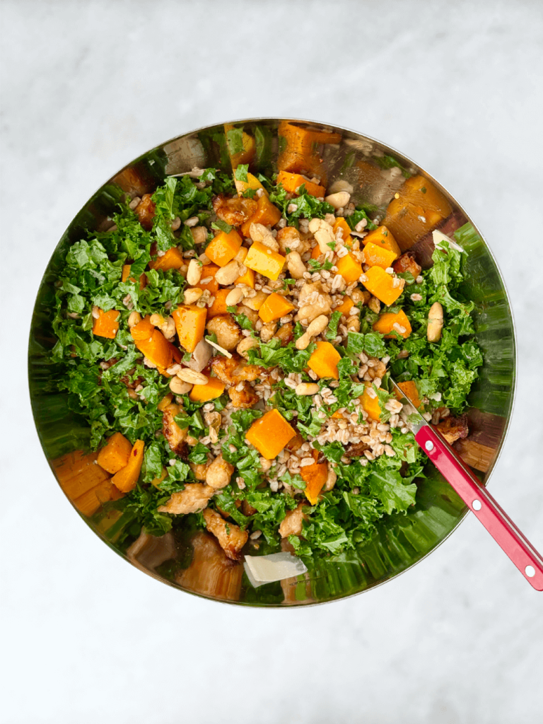 Mixing bowl of fall farro salad with butternut squash, kale, white beans, sausage, and shaved parmesan.