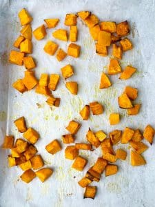 Roasted cubes of pumpkin on a parchment-lined baking sheet for warm butter bean salad.