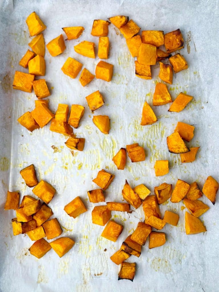 Roasted cubes of pumpkin on a parchment-lined baking sheet for warm butter bean salad.