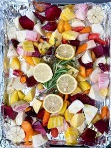 Colorful beets, carrots, parsnips, lemon, and garlic arranged on a foil-lined baking sheet before roasting.