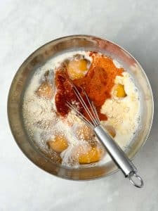 Bowl of eggs, almond milk, and spices being whisked together for a sausage and sweet potato breakfast casserole.
