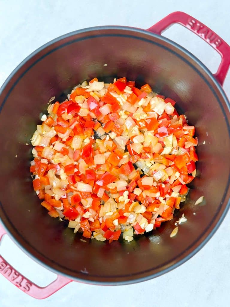 Diced onion, red bell pepper, and garlic sautéing in olive oil in a red Dutch oven for high-protein taco soup.