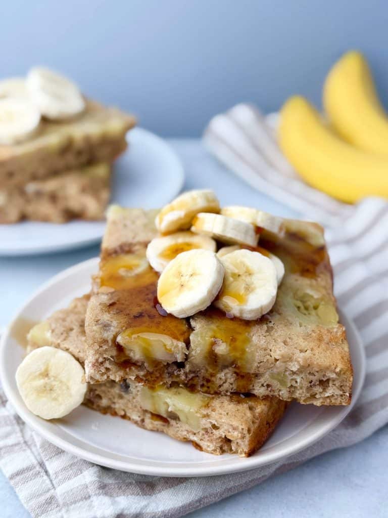 Slices of sheet-pan banana protein pancakes topped with banana slices and maple syrup.