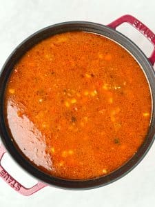 High-protein beef taco soup simmering in a red Dutch oven with a smoky tomato-chili broth and corn visible on top.