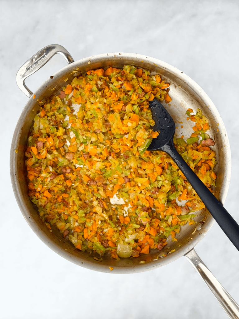 Onion, celery, carrot, and garlic mixture sautéing in a skillet until soft and fragrant for homemade lasagna sauce.