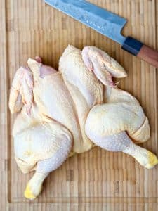 Raw whole chicken spatchcocked on a wooden cutting board with kitchen knife before seasoning.