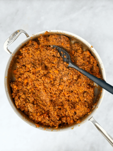 Thickening bolognese sauce halfway through simmering, showing rich tomato and meat base.