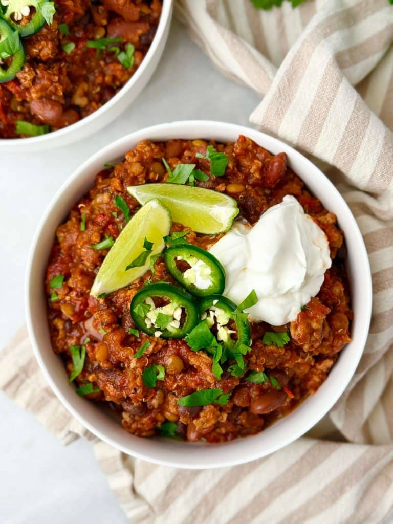 Healthy high protein chili with Greek yogurt, cilantro, and fresh lime served in a white bowl.