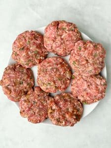 Uncooked turkey breakfast sausage patties shaped and ready to cook on a white plate.