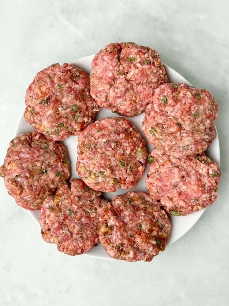 Uncooked turkey breakfast sausage patties shaped and ready to cook on a white plate.