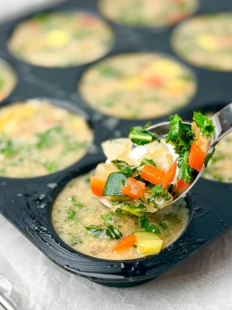 Spoonful of colorful kale, zucchini, and bell pepper filling going into muffin tin for dairy-free frittata cups