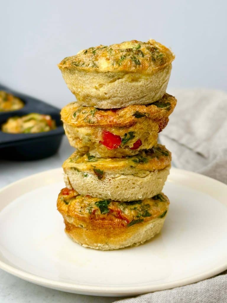 Stack of veggie-loaded dairy-free frittata cups with spinach and bell pepper on a white plate.