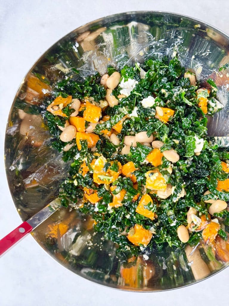 Kale, roasted pumpkin, and butter beans being tossed together with goat cheese in a mixing bowl.