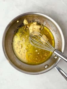 Maple Dijon dressing with toasted garlic being whisked in a small saucepan for warm butter bean salad.