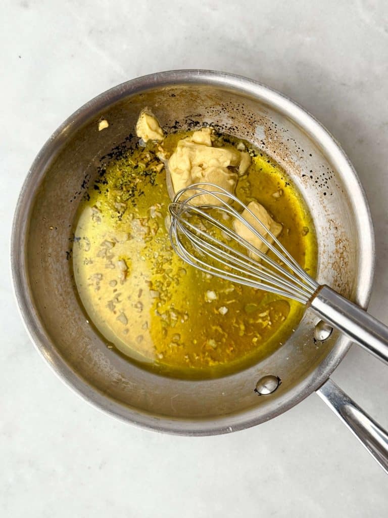 Maple Dijon dressing with toasted garlic being whisked in a small saucepan for warm butter bean salad.