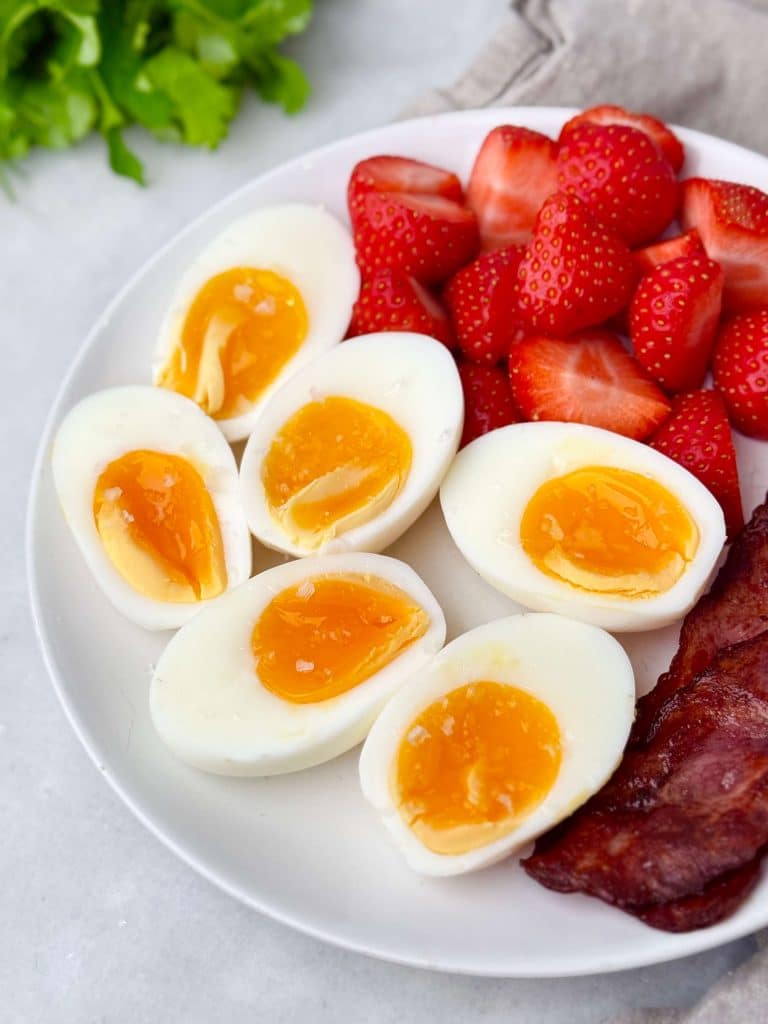 Plate of soft-boiled eggs with runny yolks, crispy turkey bacon, and fresh sliced strawberries for a balanced high-protein low-calorie breakfast.