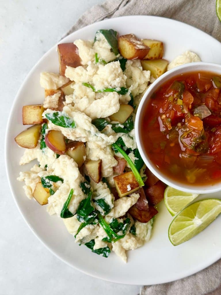 Plate of egg white scramble with spinach and roasted potatoes, served with salsa and lime wedges for a healthy high-protein low-calorie breakfast.