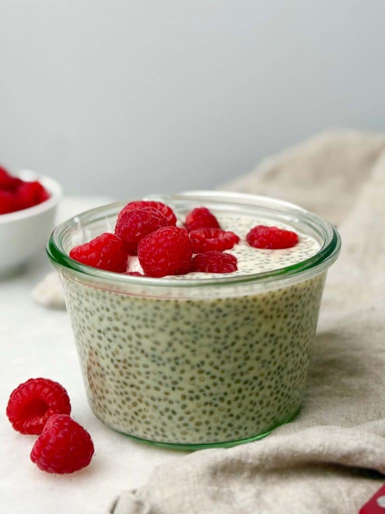 Glass jar filled with creamy protein chia seed pudding topped with fresh raspberries, set on a neutral background for a healthy high-protein 300-calorie breakfast idea.