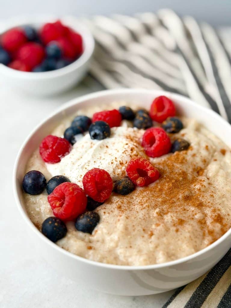 Bowl of creamy protein oats made with egg whites, topped with Greek yogurt, fresh raspberries, blueberries, and a sprinkle of cinnamon for a high-protein 300-calorie breakfast.