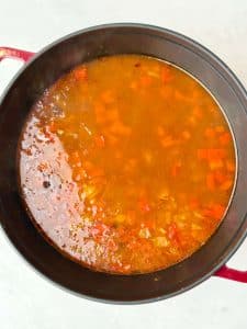 Pot of black bean soup base simmering with broth, onions, and peppers.