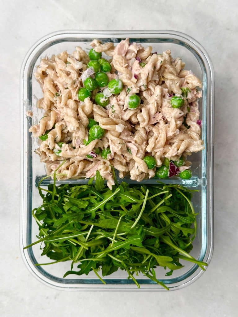 Glass meal prep container filled with high-protein tuna pasta salad with peas and fresh arugula on the side.