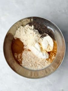 Overhead view of cinnamon roll overnight oats ingredients in a bowl, including rolled oats, cinnamon, chia seeds, Greek yogurt, protein powder, and almond milk before mixing.
