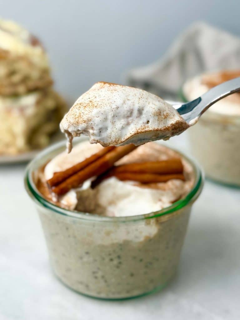 Close-up of a spoonful of creamy cinnamon roll overnight oats with yogurt frosting and cinnamon, lifted from a glass jar.