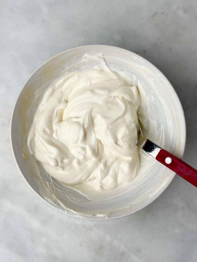 Bowl of creamy yogurt and cream cheese frosting mixture for cinnamon roll overnight oats, stirred with a spatula.