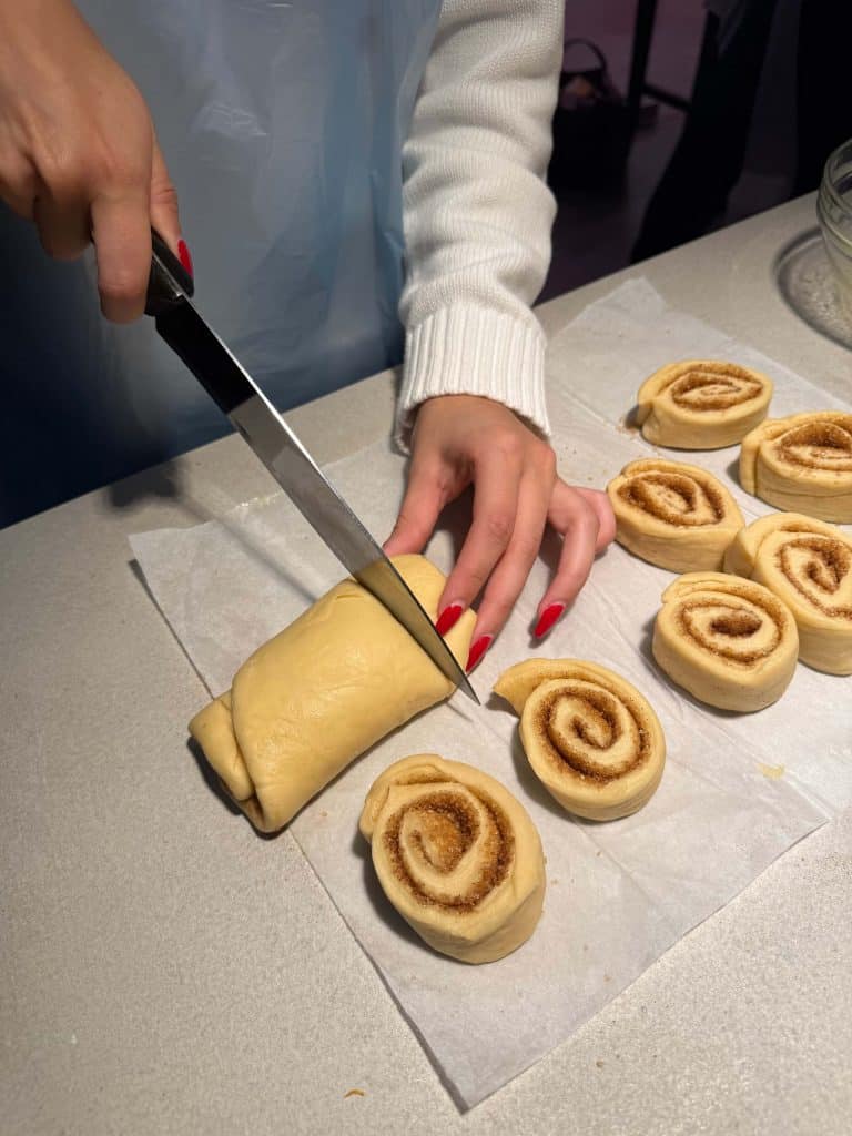 Woman cutting homemade cinnamon roll dough on a countertop for a cozy baking hobby.