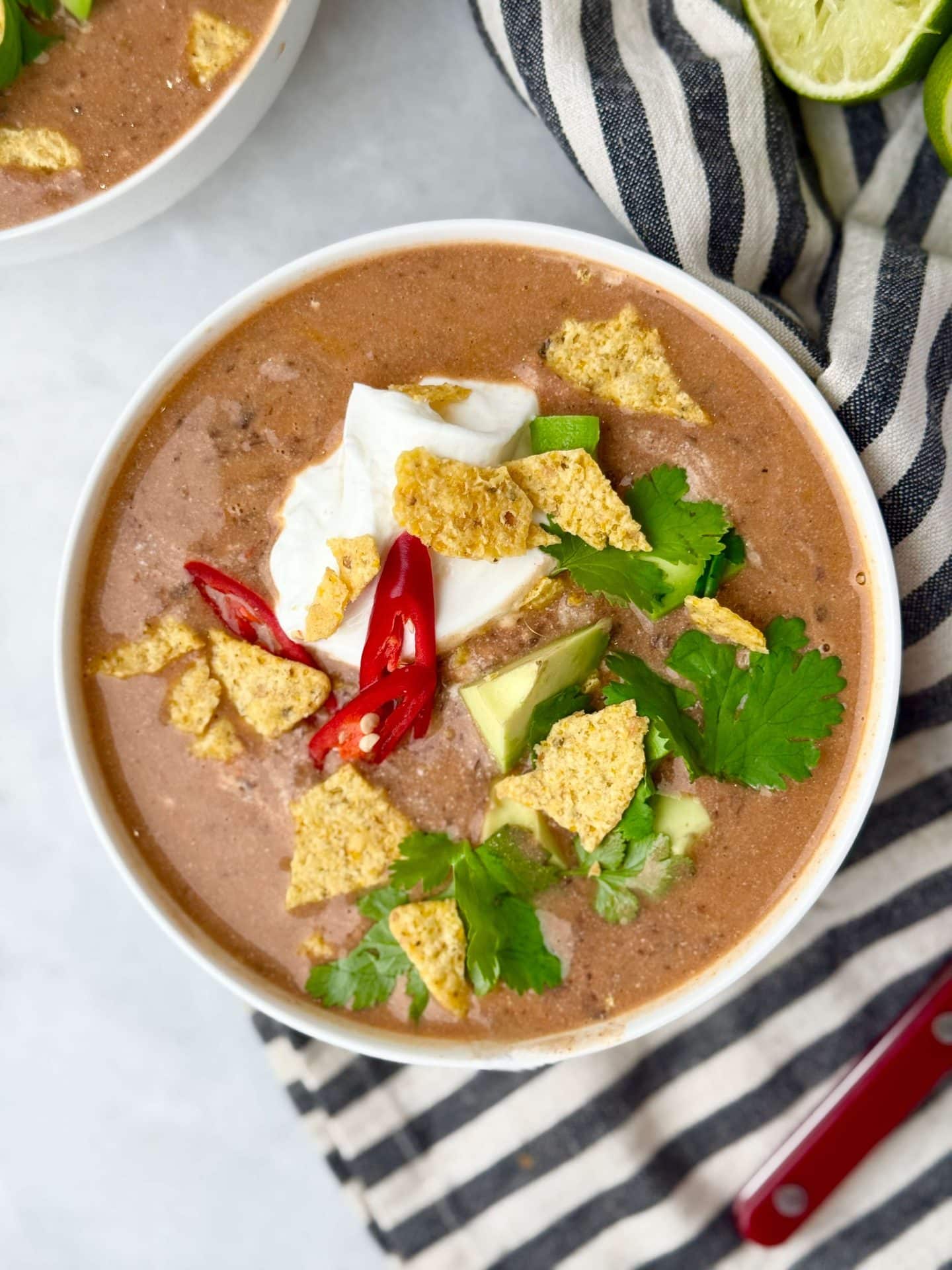 Overhead view of creamy high-protein black bean soup with yogurt, cilantro, avocado, and tortilla chips.